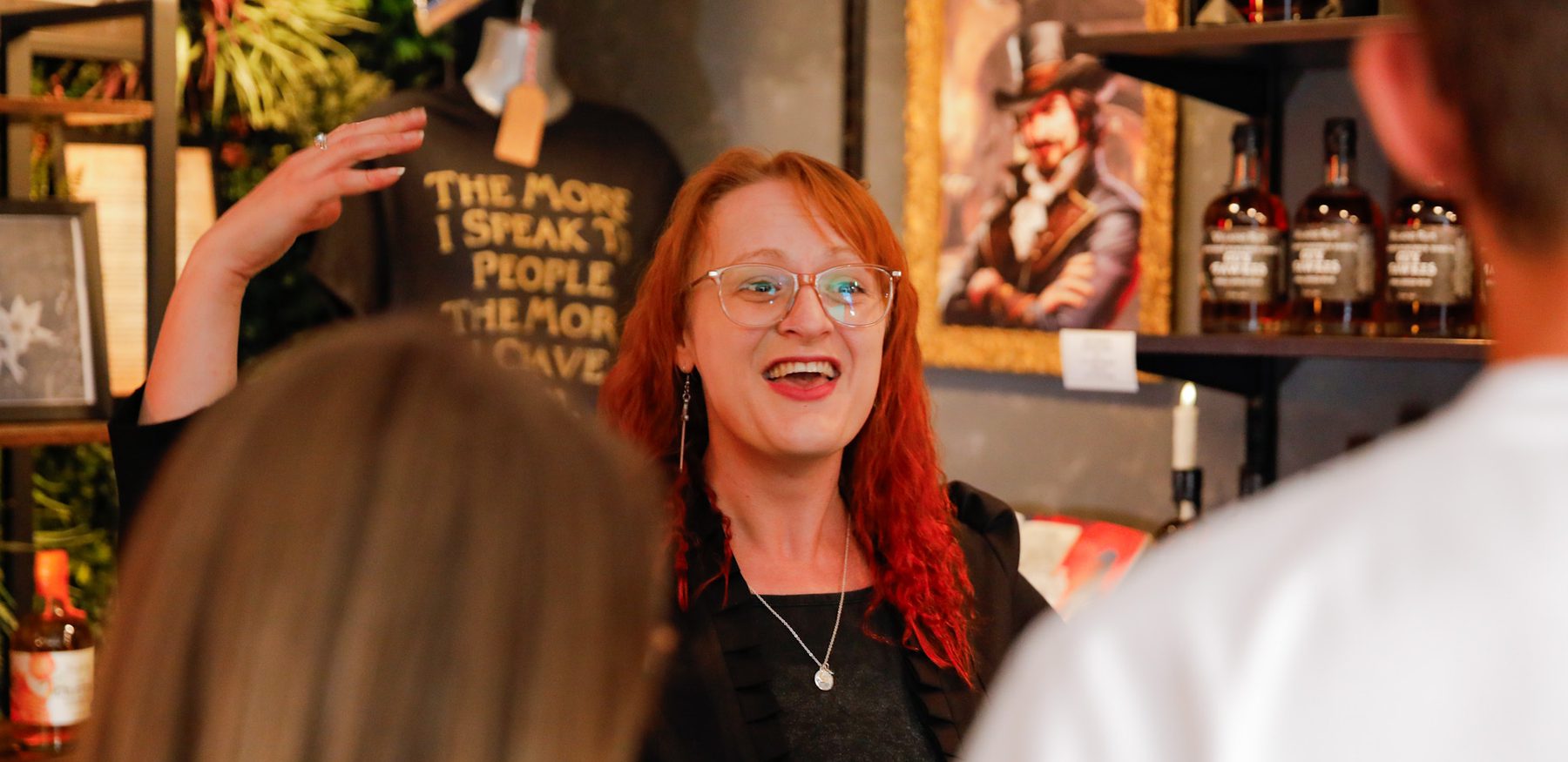 A costumed guide at Villains Rum of York leads a rum tasting inside a dimly lit shop filled with vintage decor and bottles. Guests smile and raise tasting glasses as they listen to stories of York’s historical villains.